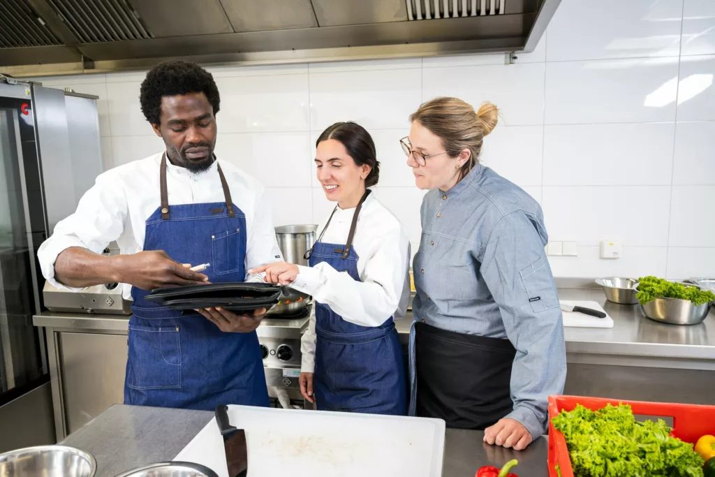 Drei Kuechenmitarbeitende schauen gemeinsam auf ein Tablet in einer Profikueche.