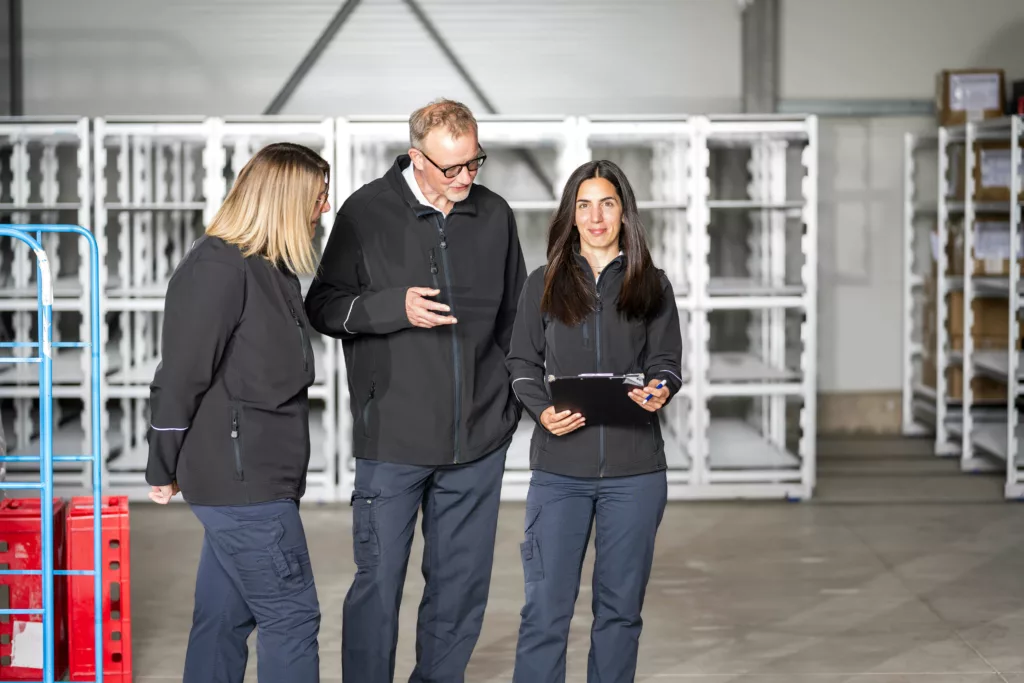 Drei Personen stehen zusammen in einem Lagerraum.
