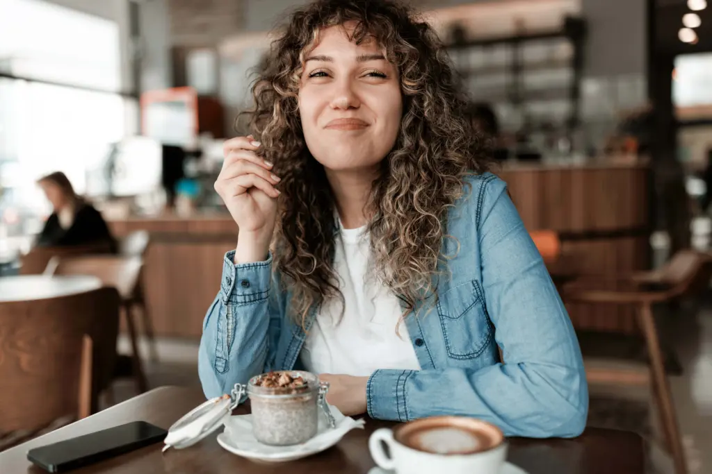Eine lockige, lächelnde Frau sitzt in einem Café.