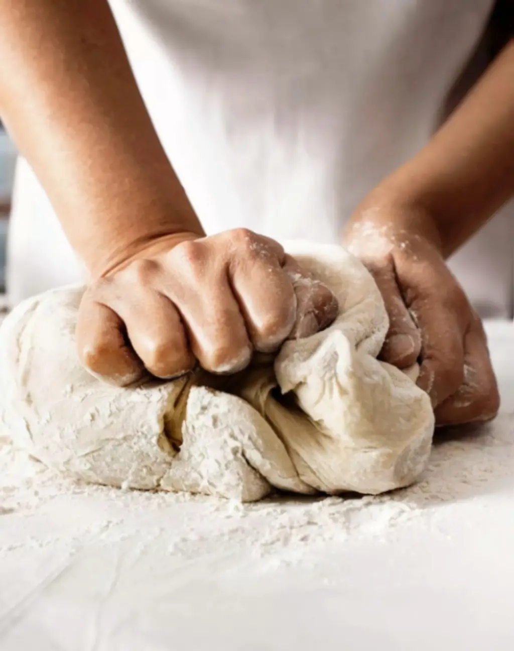 Zwei Hände kneten einen Teig auf einer Arbeitsfläche.