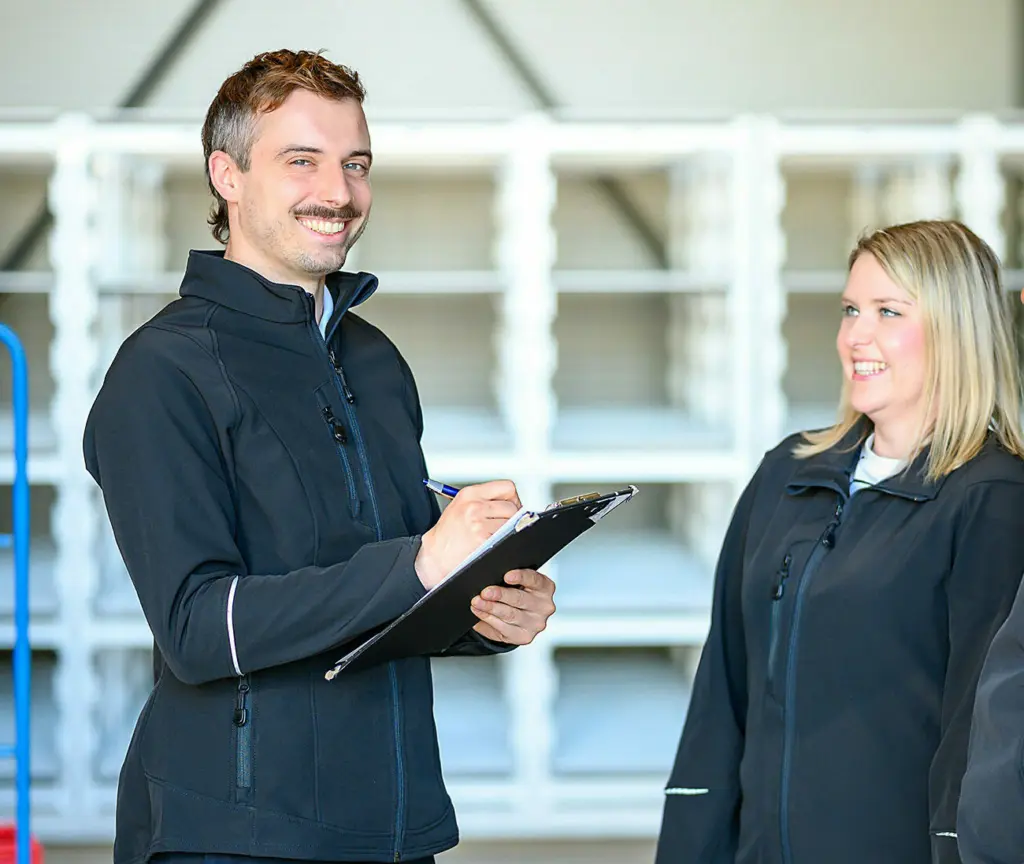 Ein Mann hält ein Klemmbrett in der Hand, neben ihm steht eine Frau.