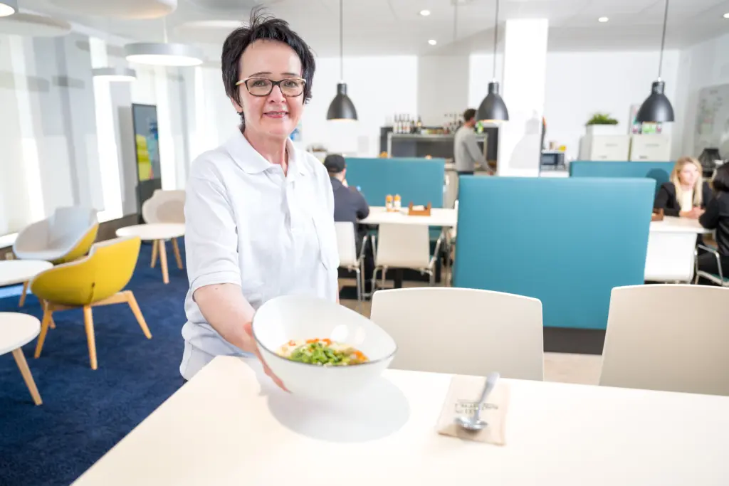 Egle steht lächelnd da und präsentiert einen frisch angerichteten Salatteller.