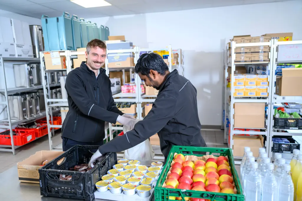 Nikolas und ein Kollege räumen gemeinsam Waren in ein Regal ein.