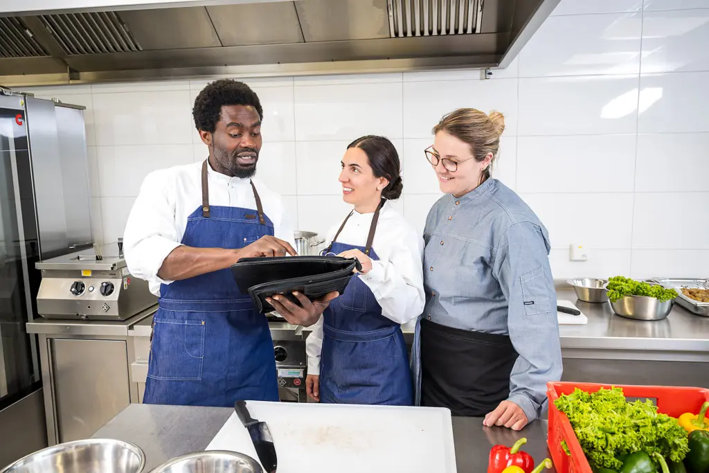 Drei Köchinnen und Köche in einer Profiküche schauen gemeinsam auf ein Tablet.