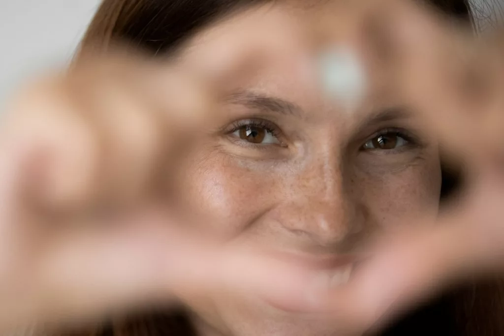 Eine Frau blickt lächelnd durch ein mit den Händen geformtes Herz.