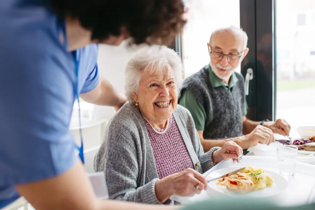 Eine ältere Dame sitzt lachend beim Mittagessen im Senior:innenheim