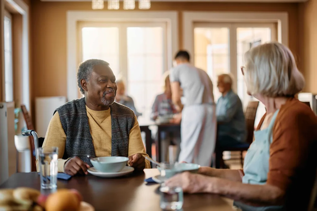Zwei Personen in einem Senior:innenheim unterhalten sich beim Essen.