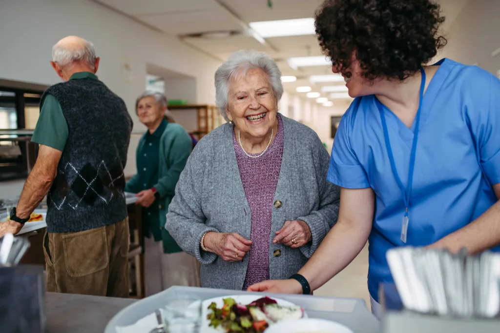 Das Pflegepersonal reicht einer strahlenden Seniorin das Essen.