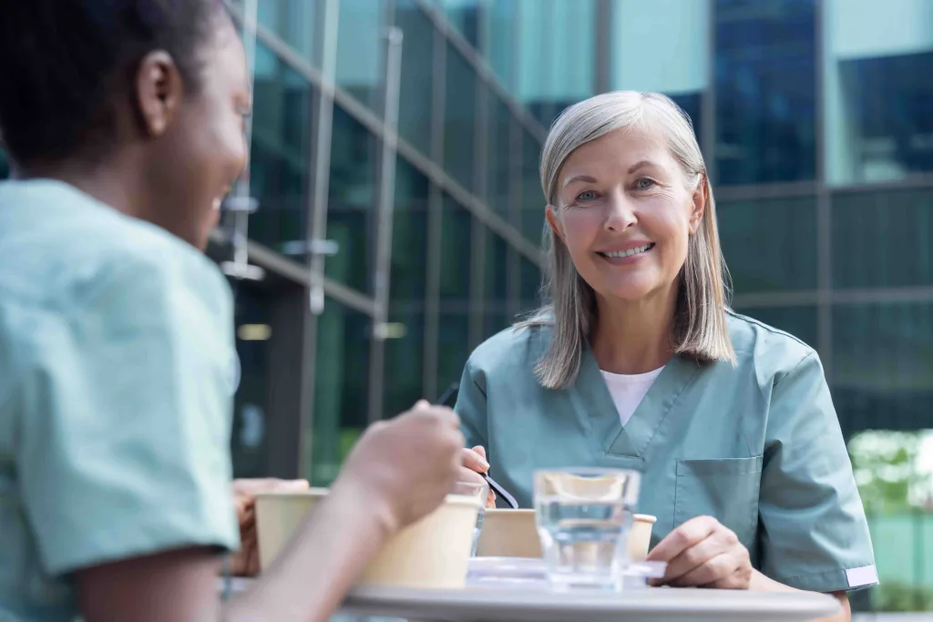 Zwei Frauen in Krankenhauskleidung genießen ihre Pause an der frischen Luft und essen Mittag.