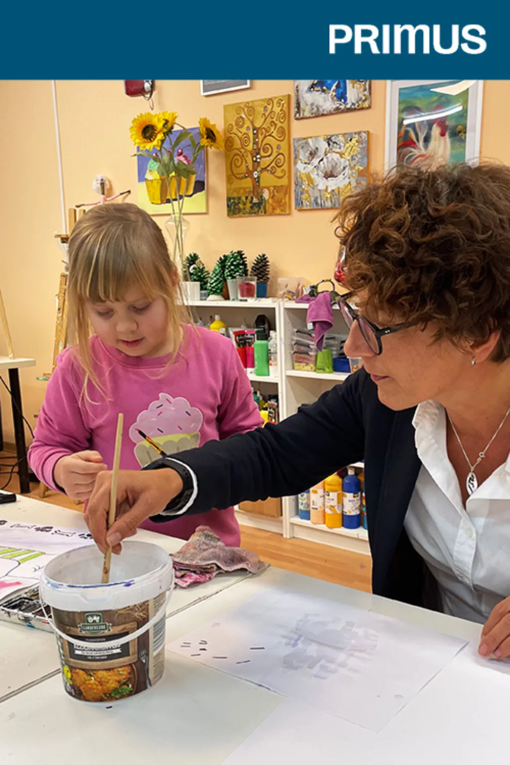 Eine Frau malt gemeinsam mit einem Kind auf einem Blatt Papier.