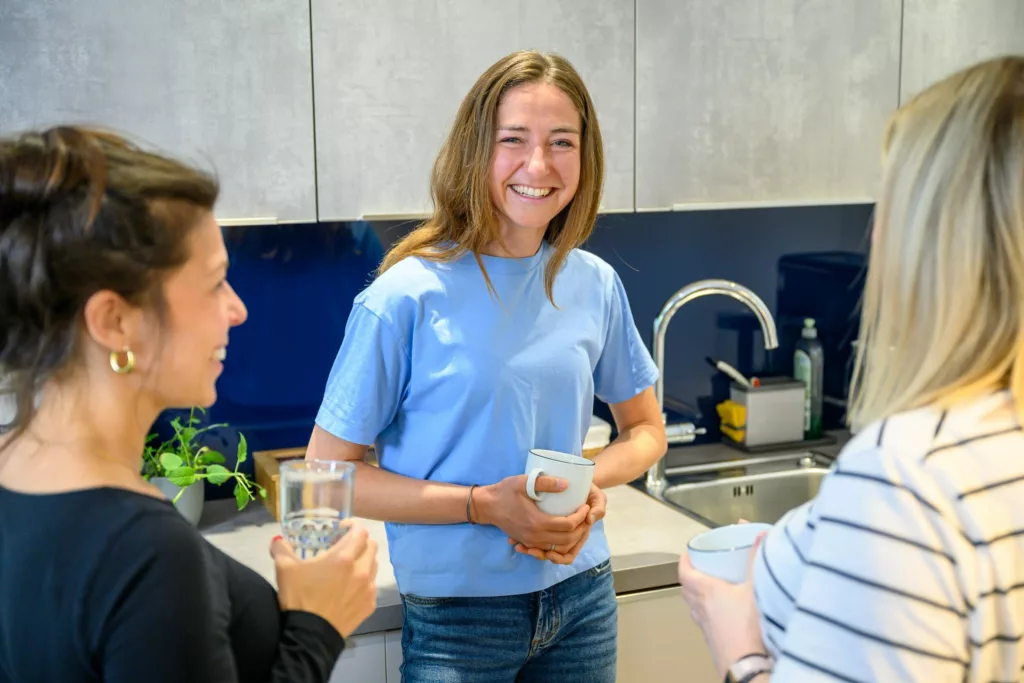 Drei Frauen stehen in einer Buerokueche und unterhalten sich bei Getraenken.