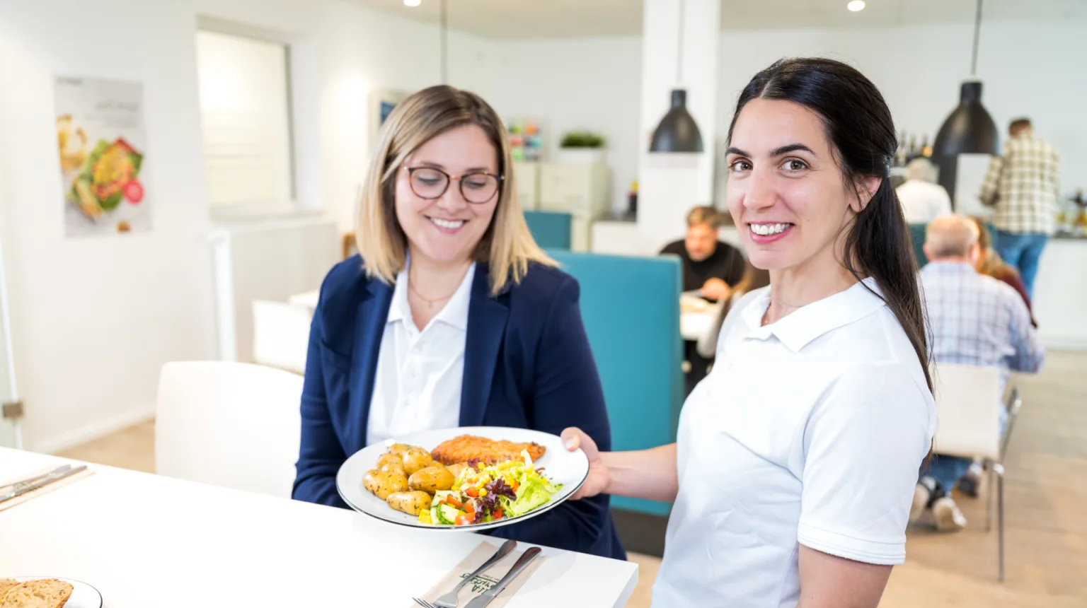 Eine Servicekraft übergibt einer Frau an einem Tisch einen Teller mit Essen.