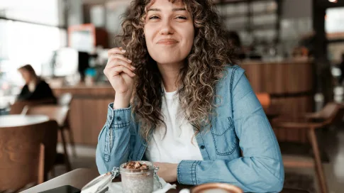 Eine lockige, lächelnde Frau sitzt in einem Café.