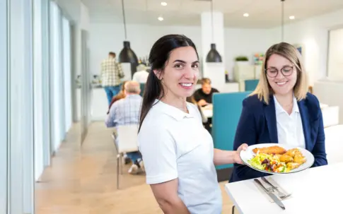 Eine Servicekraft übergibt einer Frau einen Teller mit Essen.