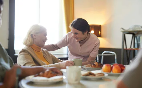 Eine Frau bedient eine Seniorin am Tisch.