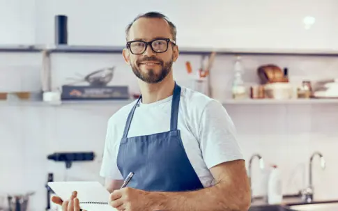 Ein Koch steht in der Küche und hält einen Schreibblock in der Hand.