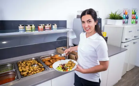 Eine Servicekraft steht vor einer Theke und hält einen Teller in der Hand.