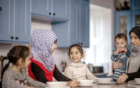 Familie sitzt in einer Küche zusammen, zwei Frauen mit Kopftuch, zwei Kinder und ein Baby